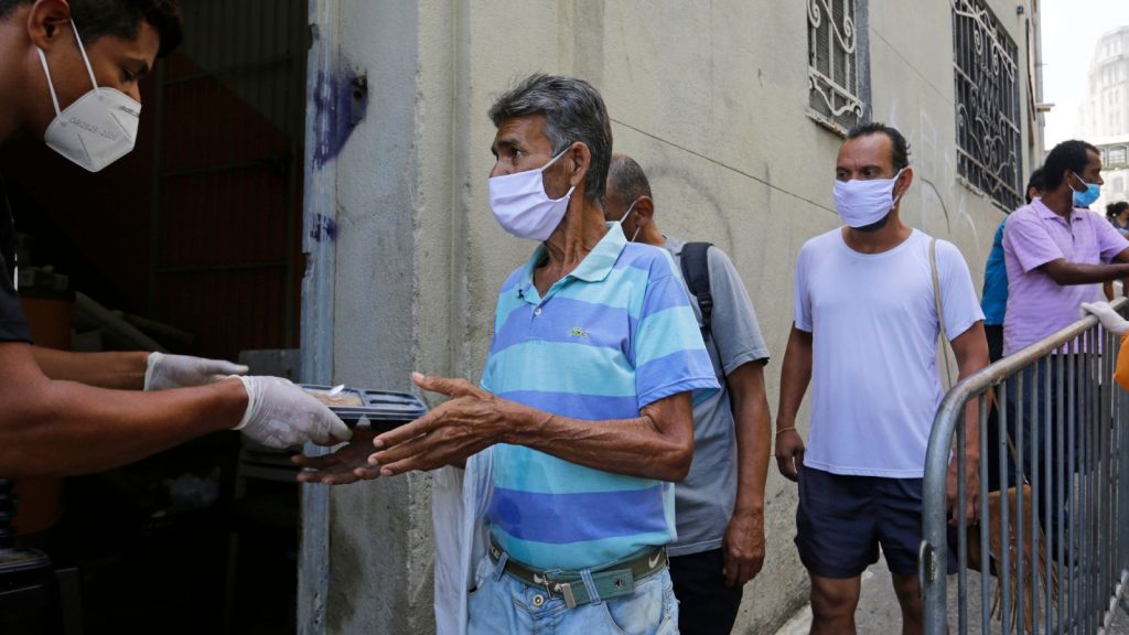 people wait in line to receive food donations for lunch in a downtown street during a severe economic crisis 