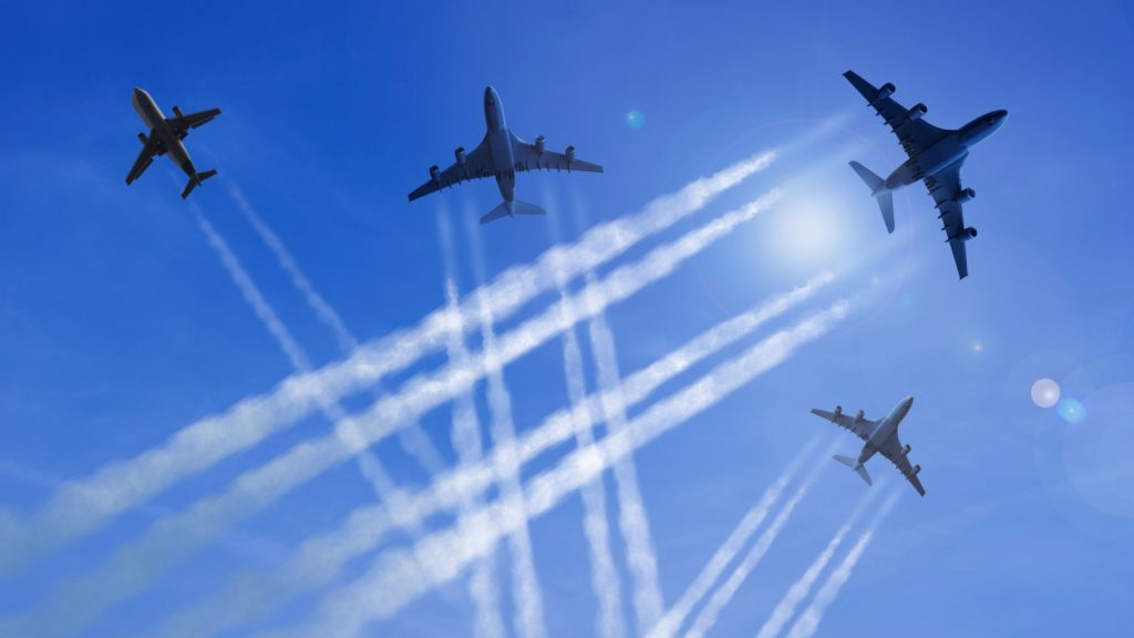 Airplanes fly against a blue sky, leaving chemtrails