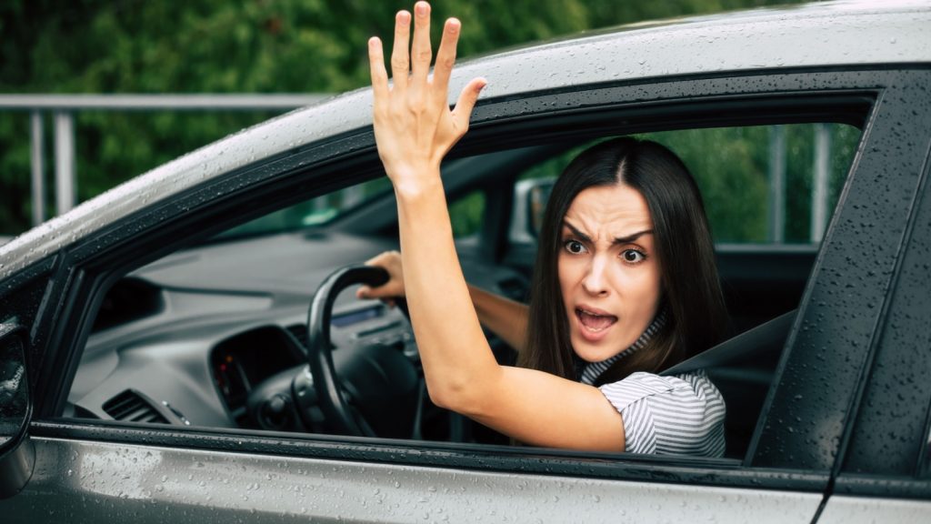 Aggressive driver. Car accident. Close up portrait displeased angry woman driving car and shouting at someone with hand fist up in air. 