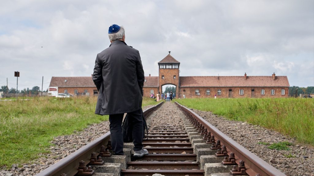 Jewish man walking toward the entrance to Auschwitz-Birkenau via the train tracks, paying his respects