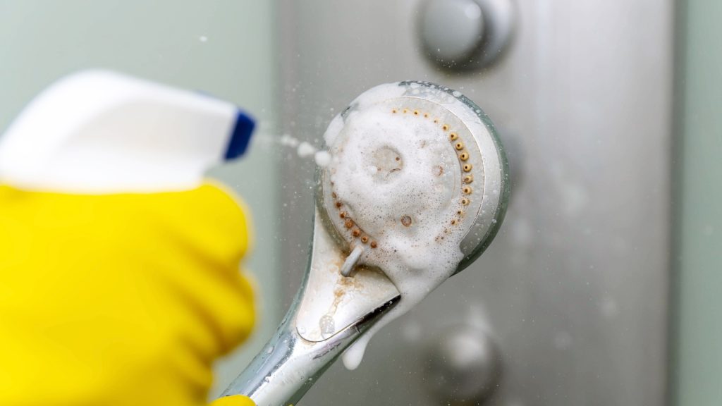 Close-up spray of cleaning agent onto the shower head. Lime deposits on the tap. vinegar usage. 