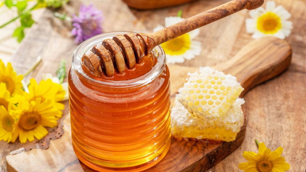 Natural organic honey in glass jar, honey dipper and honeycombs are near.