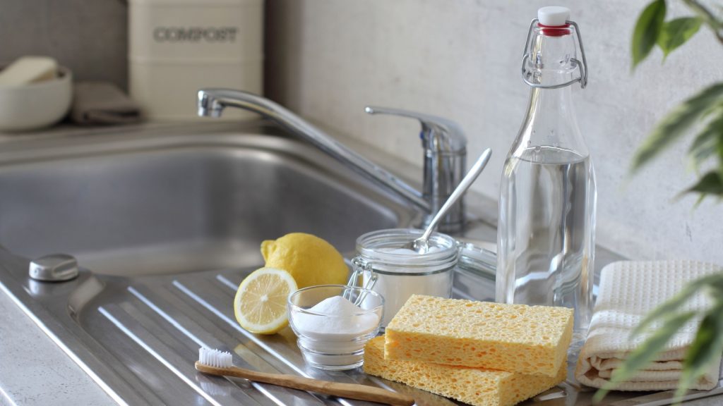 Vinegar and baking soda, lemon, natural sponge, toothbrush and towels on the kitchen sink. Natural and eco-friendly cleaning products.