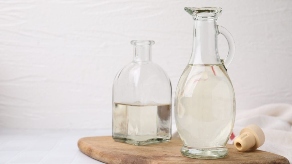 Vinegar in glass jug and bottle on white table.