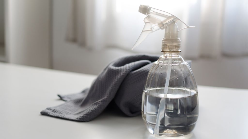 Spray bottle filled with pure water and vinegar and a cleaning cloth on a table against a bright window all in white and gray color. Environmentally friendly eco cleaning products concept. Zero waste