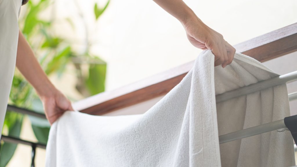 Woman put pure white towel hangs on aluminium hanger clothes rack at balcony, airing. 