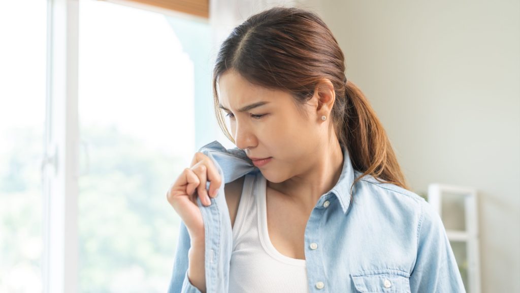 Bad smell nose concept asian young housewife woman having smelling clothes her shirt collar, sniff smelly dirty stinky musty, look disgusting from clothes after washed, laundry out of machine at home.