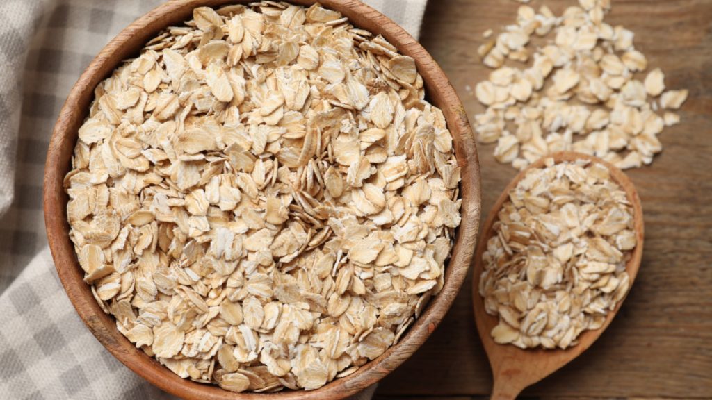 Bowl and spoon with oatmeal on wooden table, remedy, oatmeal bath