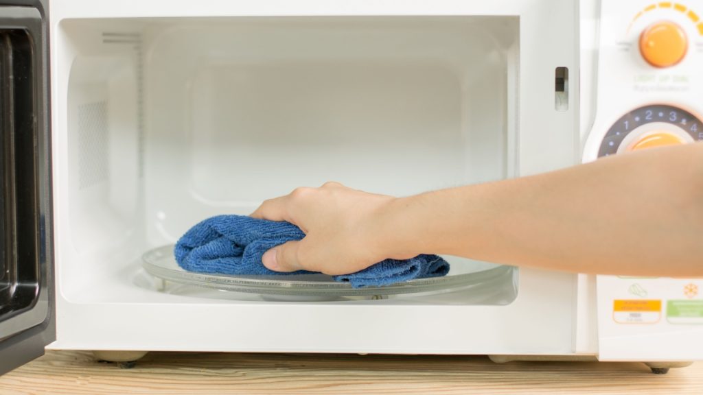 woman hand with microfiber cleaning rag wiping inside of microwave oven.