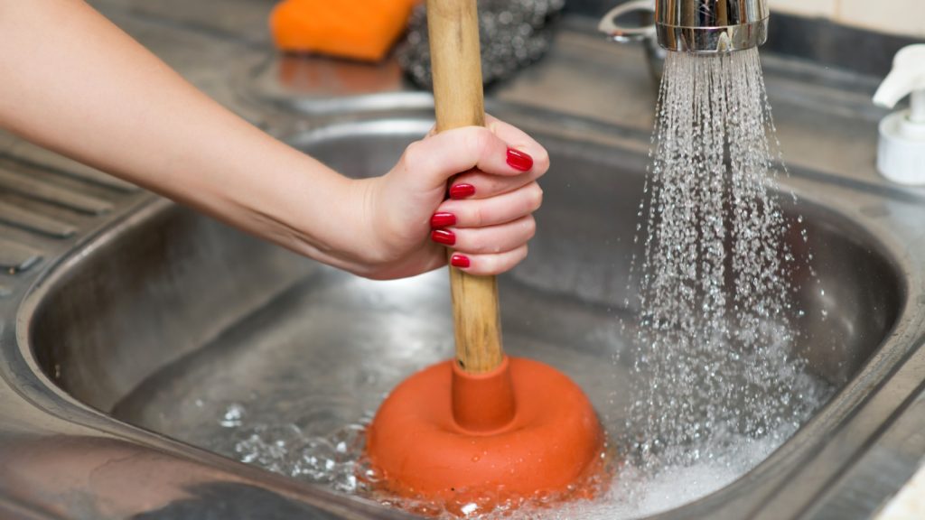 woman cleans plunger with clogged sink.