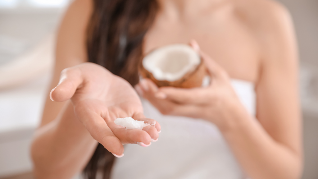 Beautiful young woman applying coconut oil on her hair at home