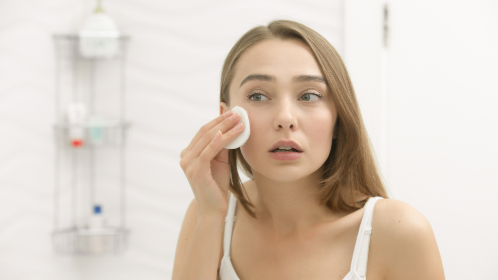 Focused beautiful young woman cleaning her skin with a cotton pad