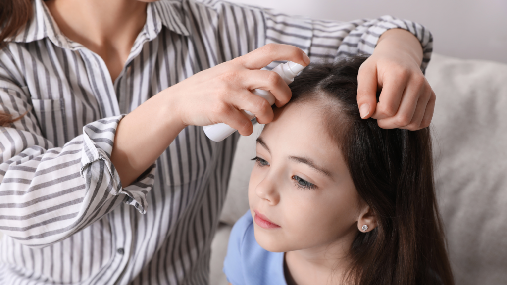 Mother using lice treatment spray on her daughter's hair indoors