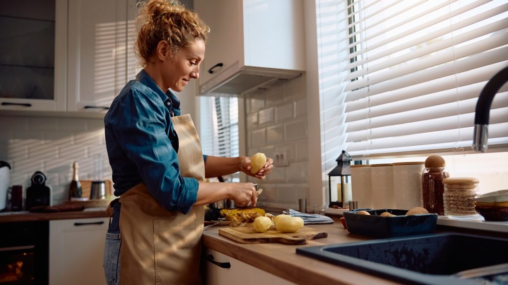 Woman in kitchen peeling a potato