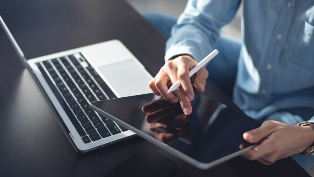 A man working on a laptop and checking his tablet