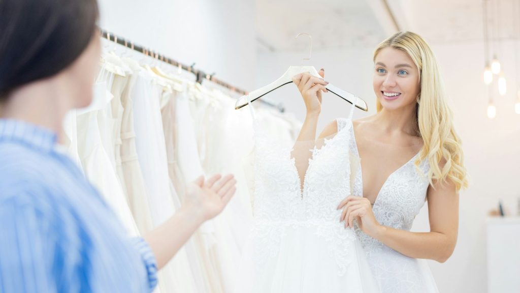 Excited beautiful bride showing pre-loved wedding dress to friend