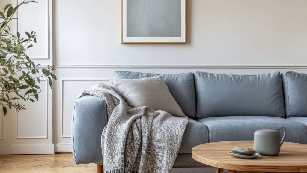 Grey sofa with a blanket, a pillow, a wooden coffee table and a plant on a wooden floor in a minimalist interior