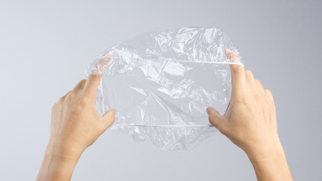 Hand holding disposable transparent plastic shower cap