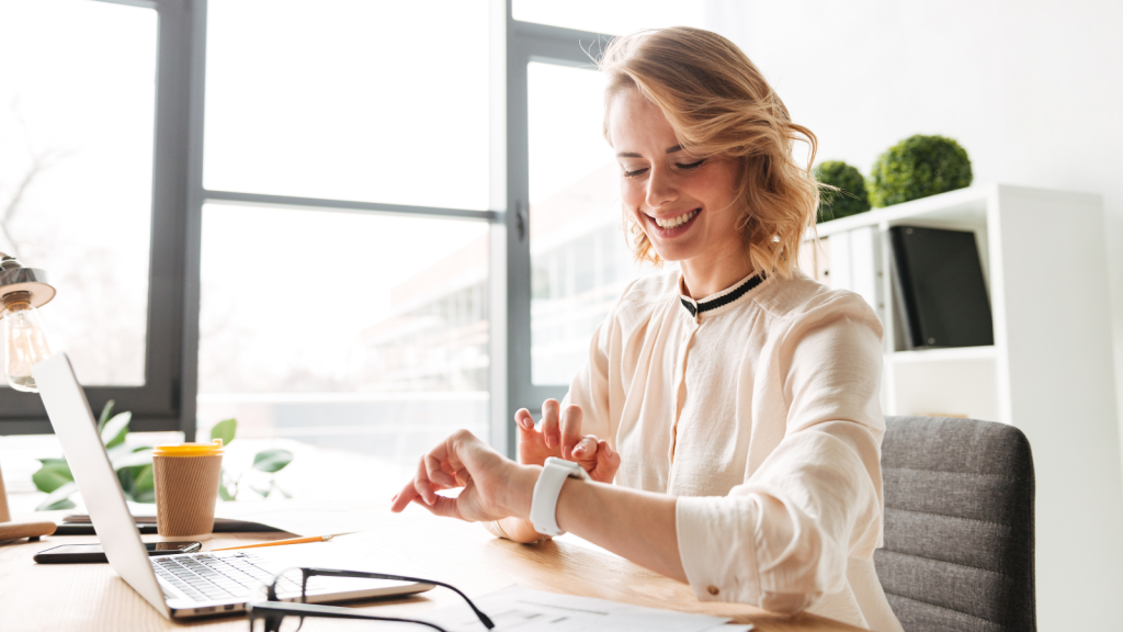 Image of cheerful young business woman sitting in office using laptop computer looking at watch