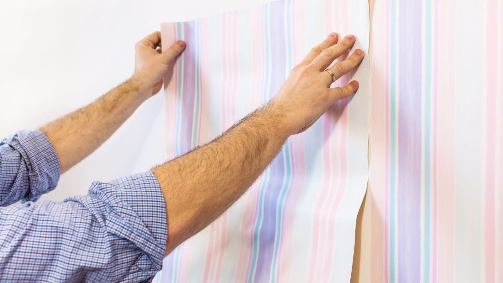 Man putting up wallpaper on the white walls