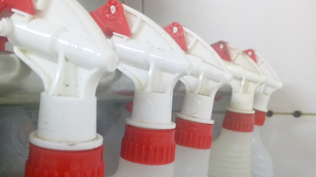 Plastic spray bottles arranged hanging on rod under sink