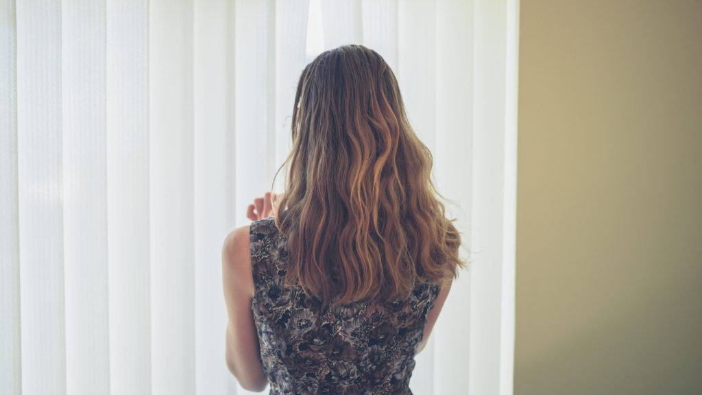 a woman peaking through the blinds at home 
