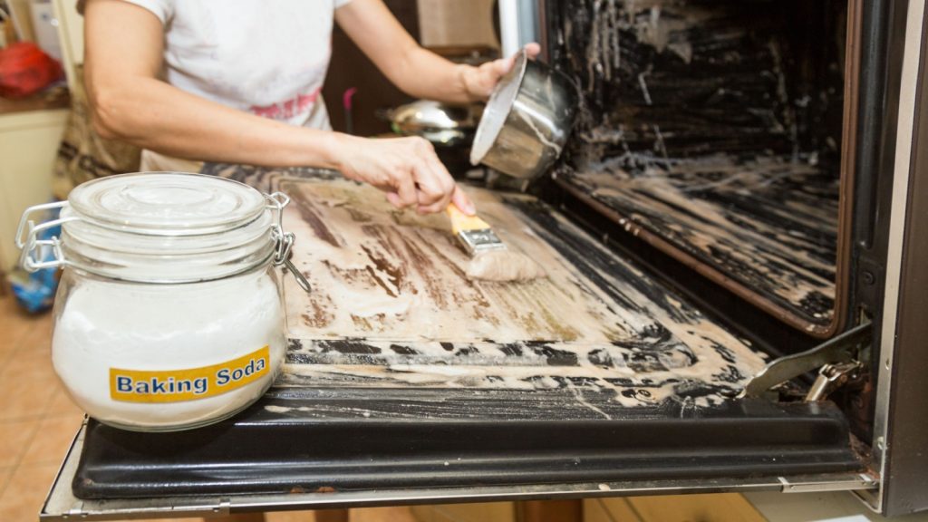 Scrubbing an oven with baking soda paste.