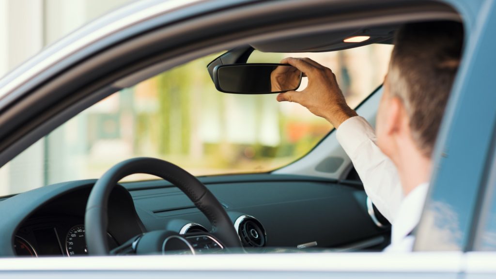 a man sitting in a car adjusting rear-view mirror
