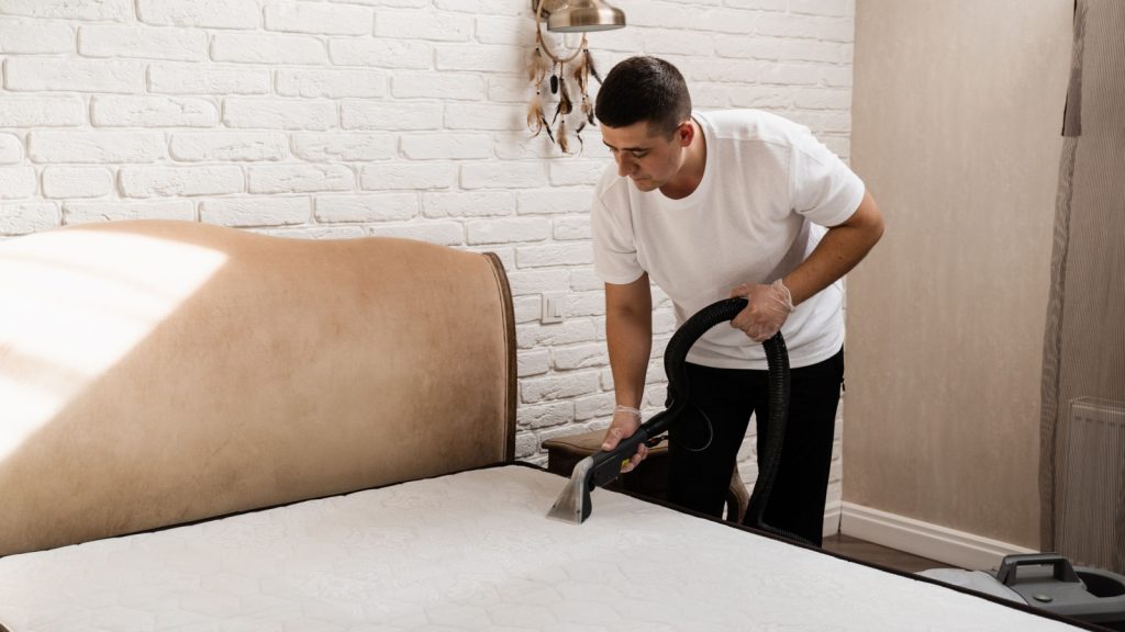 A man vacuuming a mattress.