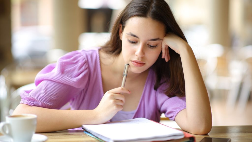 Woman thinking while looking at notebook and holding a pen