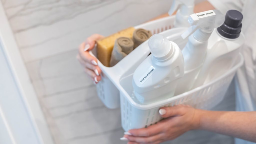 a woman's hand holding a caddy full of cleaning items