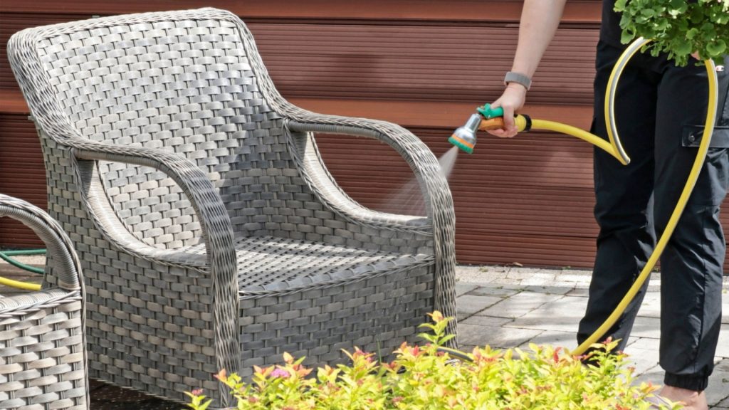 A person cleaning a patio chair with a garden hose.