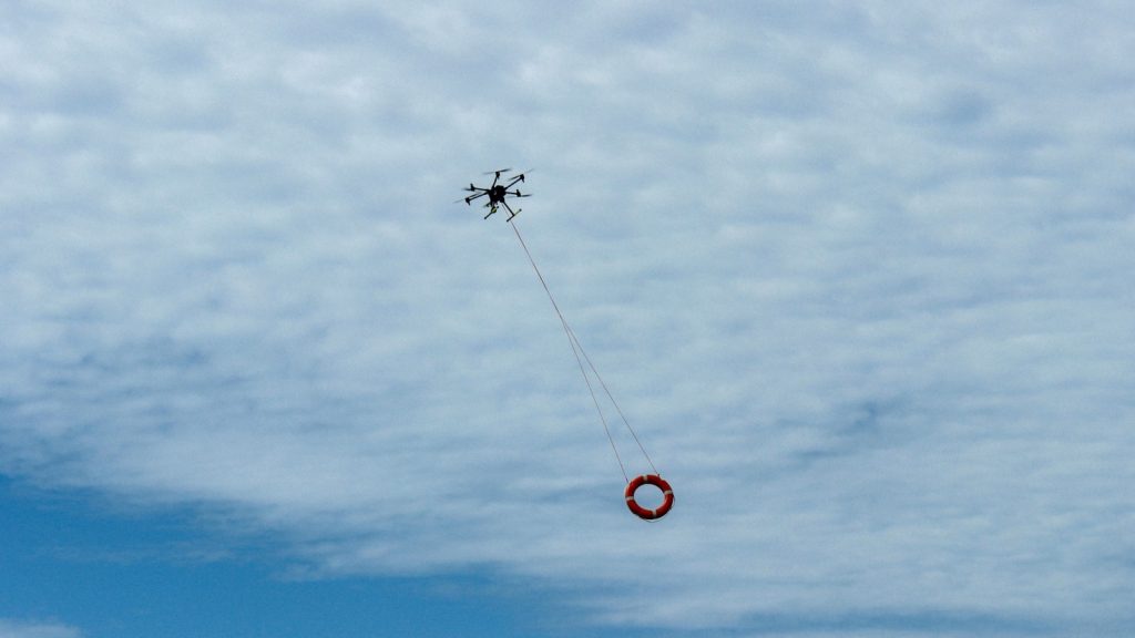 powerful rescue drone in action over the beach, lifting a lifebuoy to assist drowning individuals in the sea