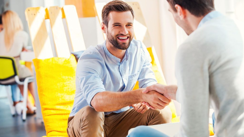 Two happy young men shaking hands while sitting in a restaurant