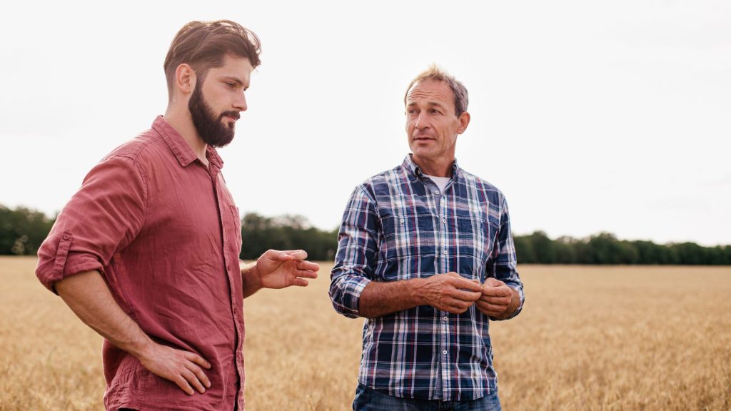 Two men are talking outside in a field background