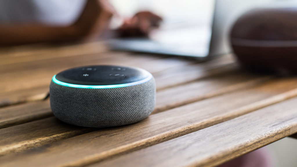 Smart speaker placed on table near crop black female using laptop at home