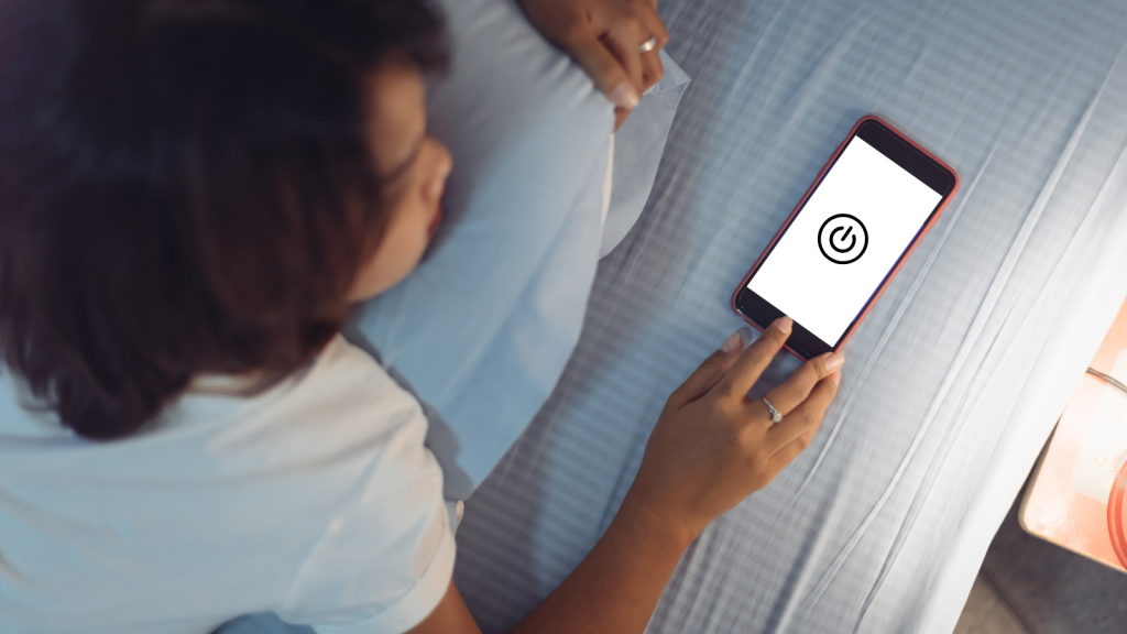 Woman turning off phone on bed