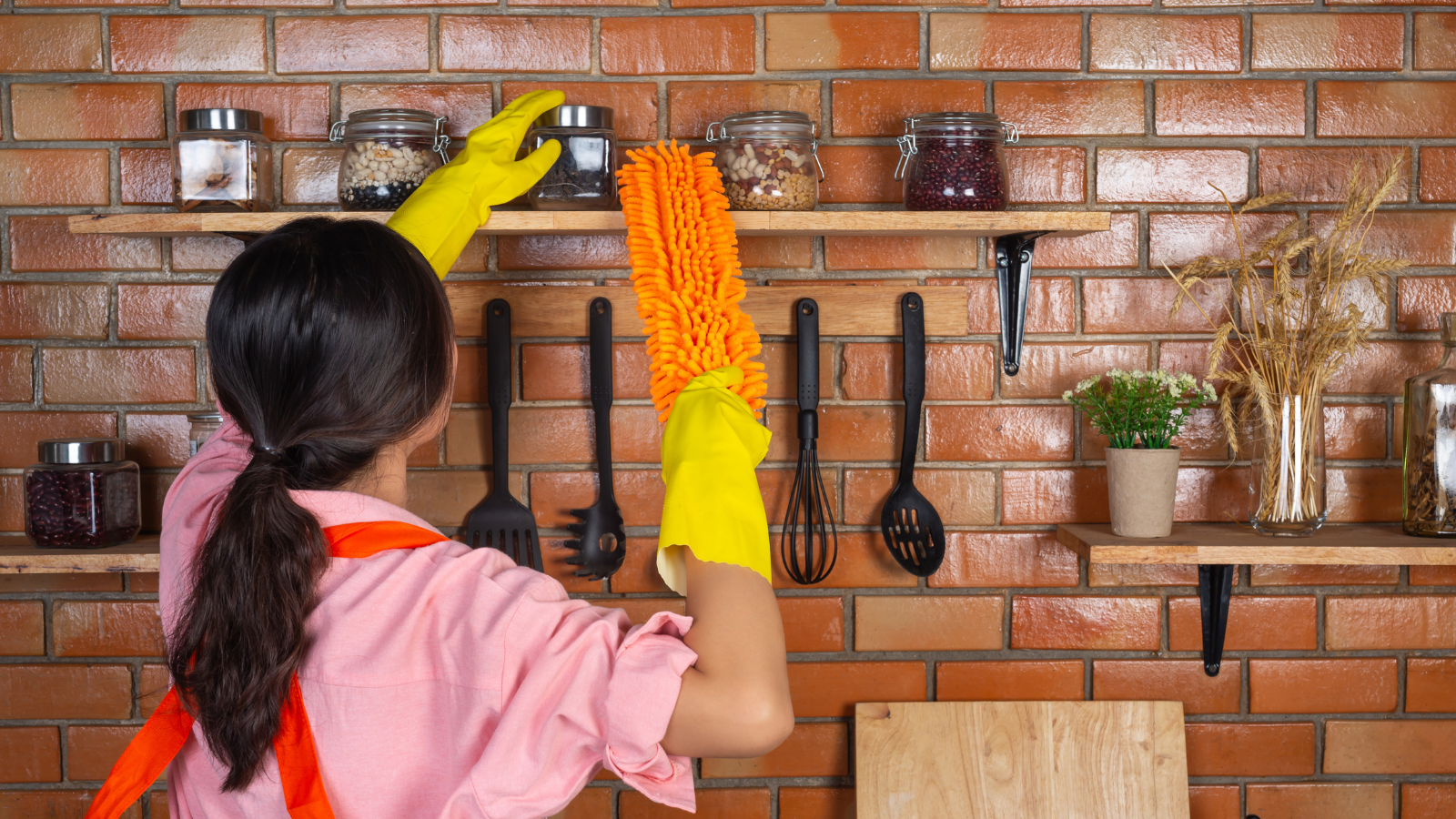 Woman holding a duster and cleaning the kitchen