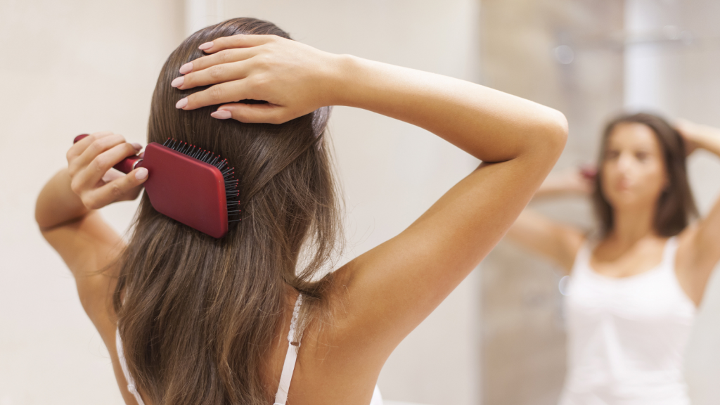 Young woman brushing healthy hair in front of a mirror