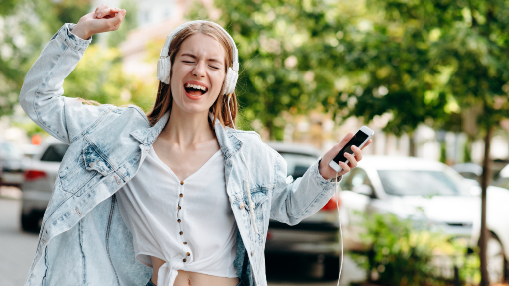 Excited girl with close eyes and smartphone listen to music in an earphones and sings outdoor