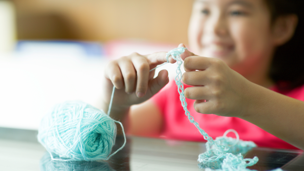 A kid sitting while holding woolen thread in hands