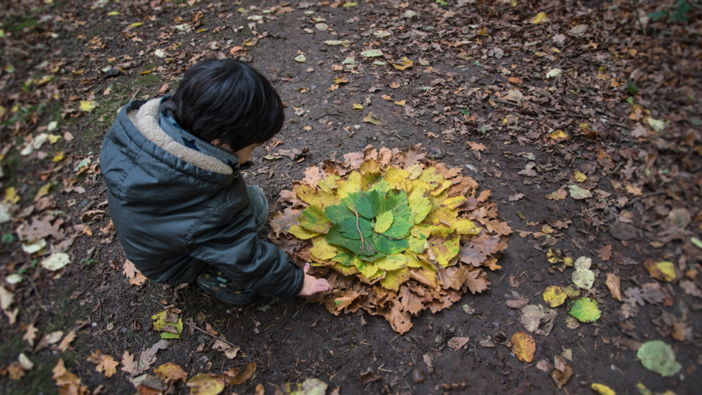 Child creating land art with multicolored autumn leaves in the forest