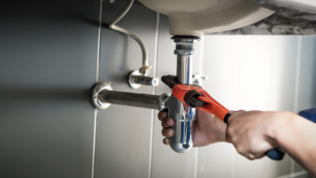 Plumber uses wrench to repair water pipe under sink