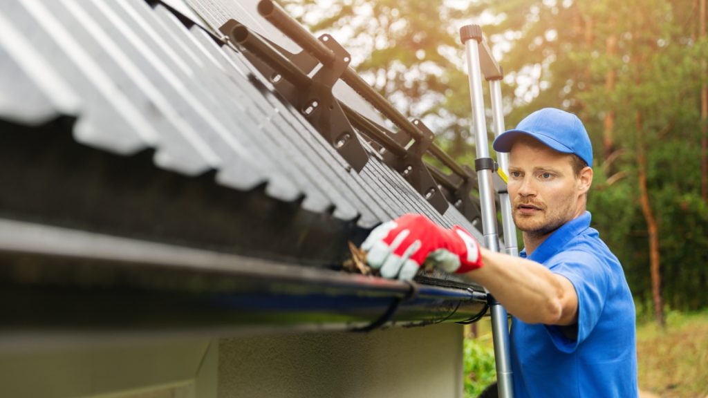 worker cleaning house gutter from leaves and dirt