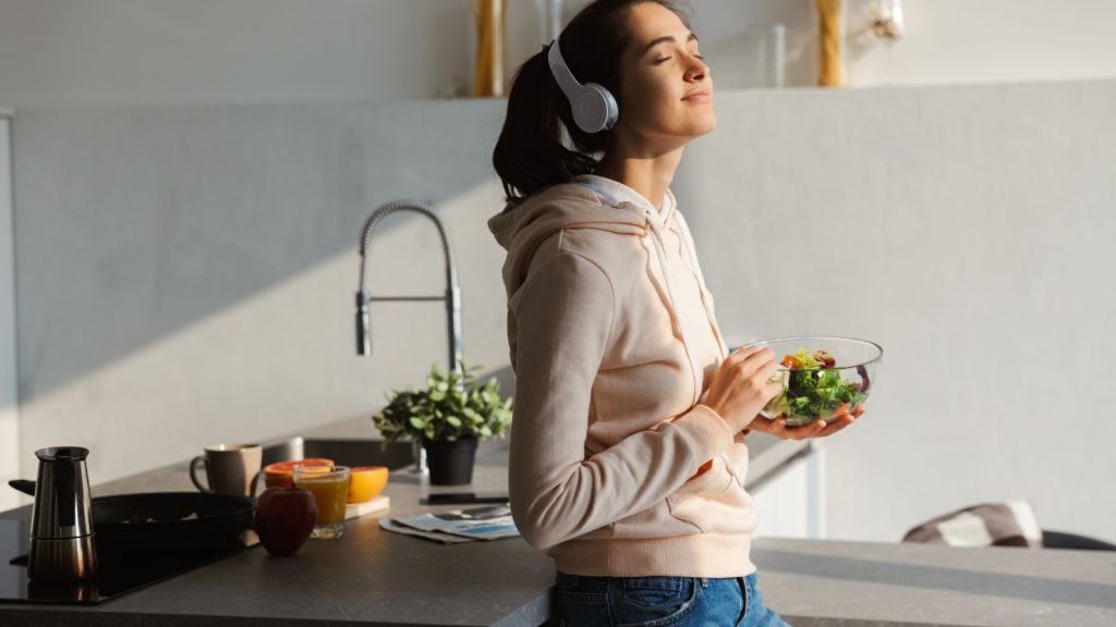 a young woman listening to music with headphones and a salad bowl in hand