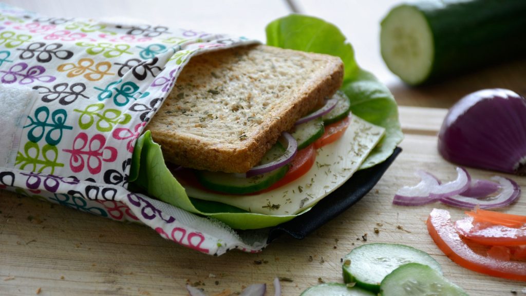 Eco-friendly durable reusable sandwich bag with healthy vegetables on a wooden cutting board.