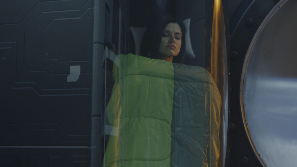 Medium shot of a young female astronaut sleeping in a glass pod in a space station