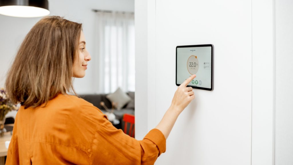 Young woman controlling temperature in the living room with a digital touch screen panel installed on the wall.