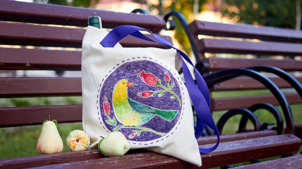 White linen eco bag decorated with painting of birds and flowers on the bench.