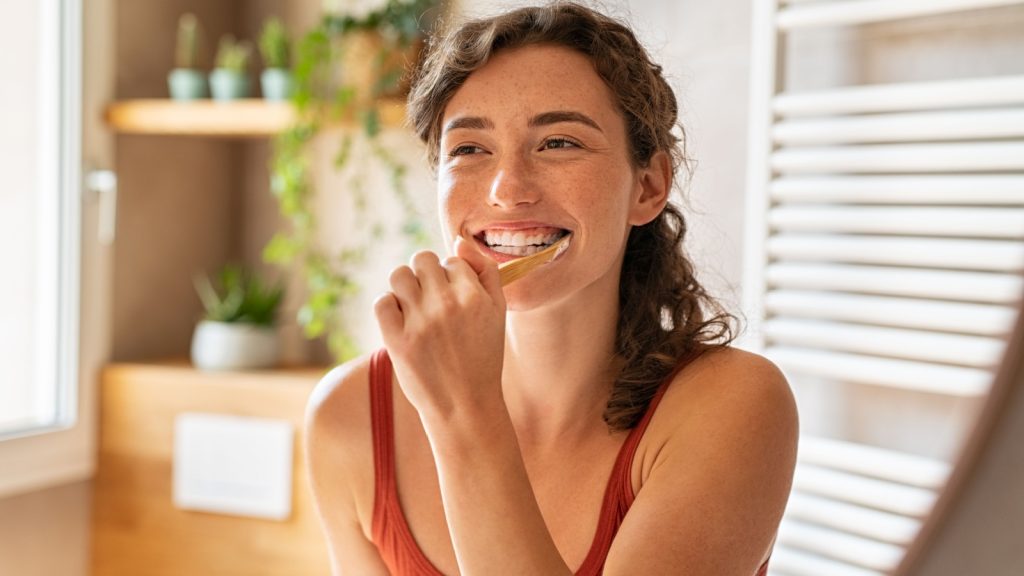 Smiling young woman brushing teeth in bathroom